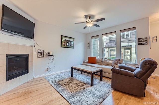 living room featuring a tiled fireplace, ceiling fan, and light wood-type flooring