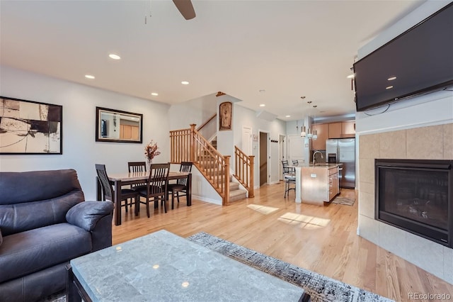 living room featuring ceiling fan, sink, a tile fireplace, and light wood-type flooring