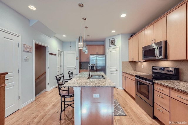 kitchen with pendant lighting, sink, stainless steel appliances, a kitchen breakfast bar, and a center island with sink