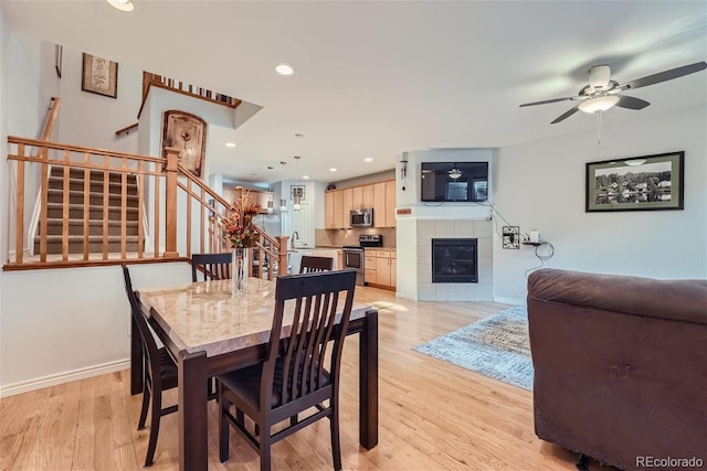 dining room featuring a tile fireplace, sink, ceiling fan, and light hardwood / wood-style floors