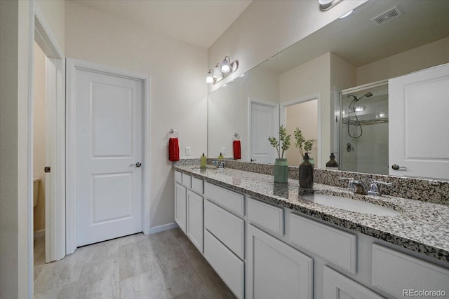bathroom with visible vents, double vanity, baseboards, a shower stall, and a sink