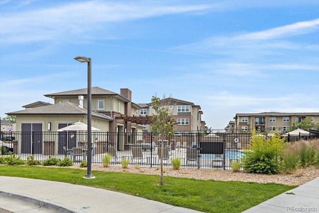 view of property's community featuring fence, a swimming pool, a lawn, and a residential view