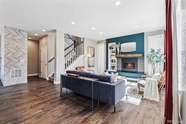 living room featuring stairs, a glass covered fireplace, visible vents, and wood finished floors