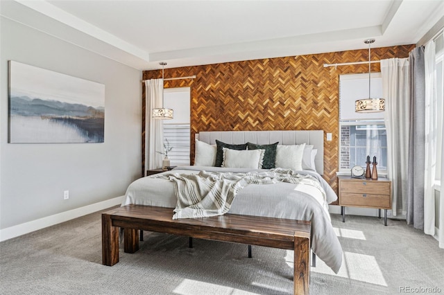 bedroom with light carpet, an accent wall, baseboards, and a tray ceiling