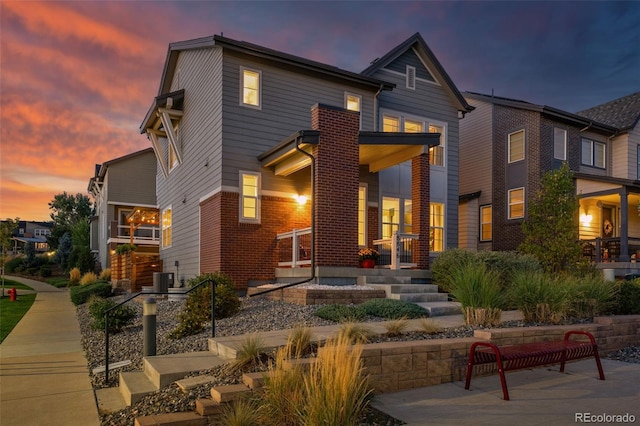 back of property at dusk featuring central AC unit, a porch, and brick siding