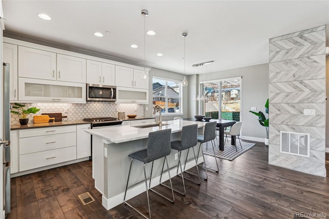 kitchen with visible vents, dark wood-style flooring, a sink, stainless steel appliances, and backsplash