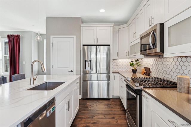 kitchen featuring tasteful backsplash, appliances with stainless steel finishes, white cabinets, a sink, and light stone countertops