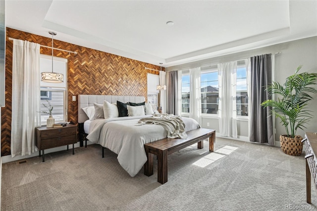 bedroom featuring an accent wall, a raised ceiling, and light colored carpet