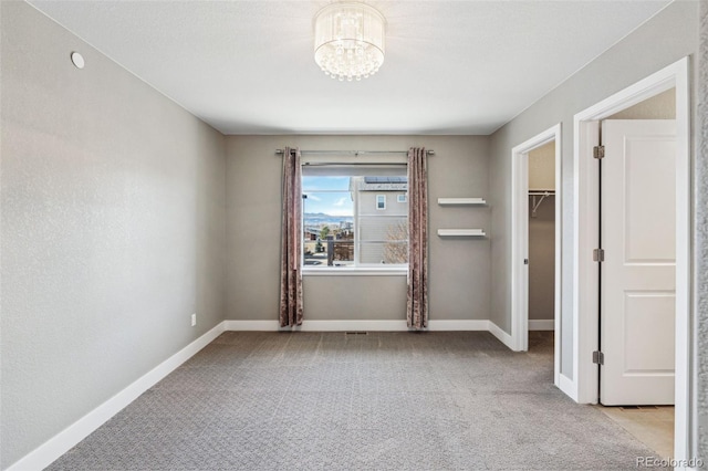 unfurnished bedroom with an inviting chandelier, a spacious closet, baseboards, and light colored carpet