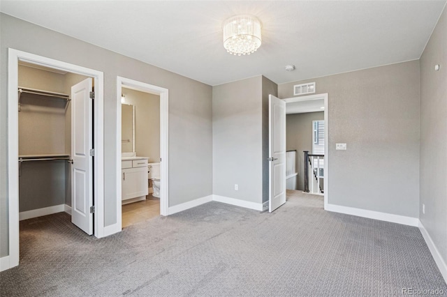 unfurnished bedroom with carpet floors, visible vents, a spacious closet, an inviting chandelier, and baseboards