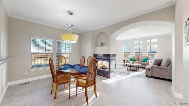 dining room with arched walkways, a multi sided fireplace, crown molding, and baseboards