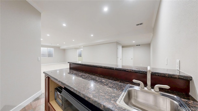 kitchen with baseboards, visible vents, dark stone counters, and a sink