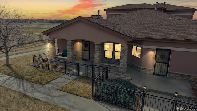 view of front of property featuring covered porch, a fenced front yard, stone siding, and stucco siding