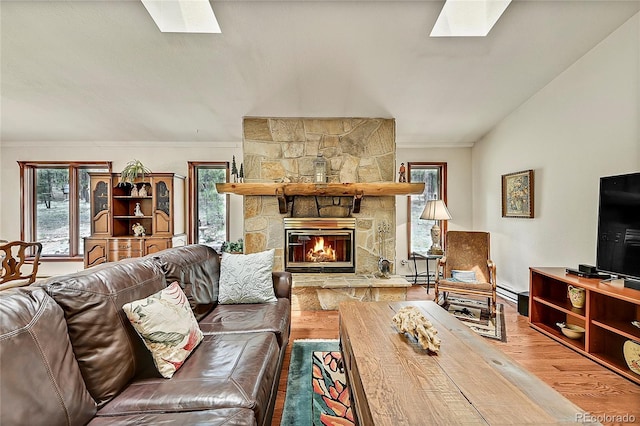 living room with hardwood / wood-style flooring, a stone fireplace, lofted ceiling with skylight, and ornamental molding