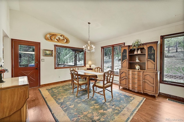 dining room with hardwood / wood-style floors, vaulted ceiling, crown molding, and an inviting chandelier