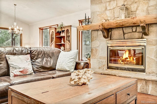 living room with light hardwood / wood-style flooring, a stone fireplace, vaulted ceiling, crown molding, and a chandelier