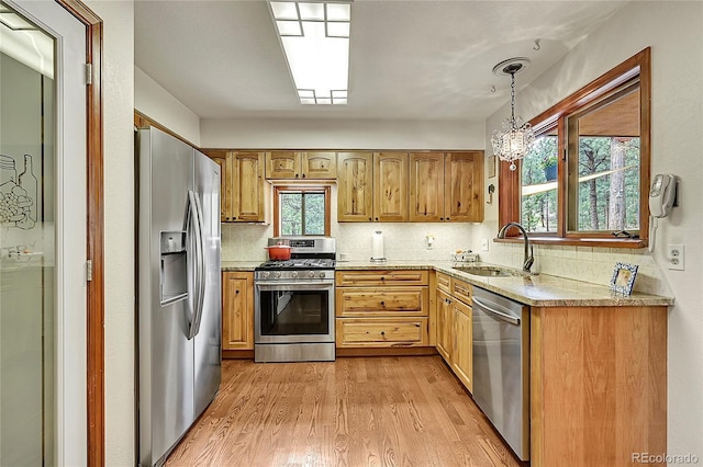 kitchen with stainless steel appliances, decorative light fixtures, light hardwood / wood-style flooring, sink, and backsplash