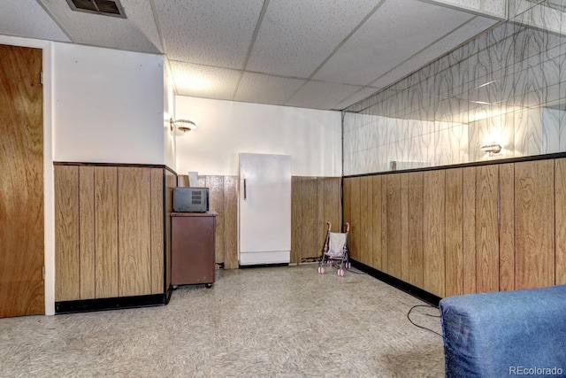 interior space featuring a paneled ceiling and wood walls