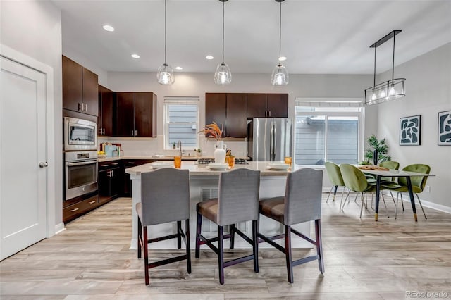 kitchen featuring dark brown cabinetry, stainless steel appliances, light countertops, a center island, and pendant lighting