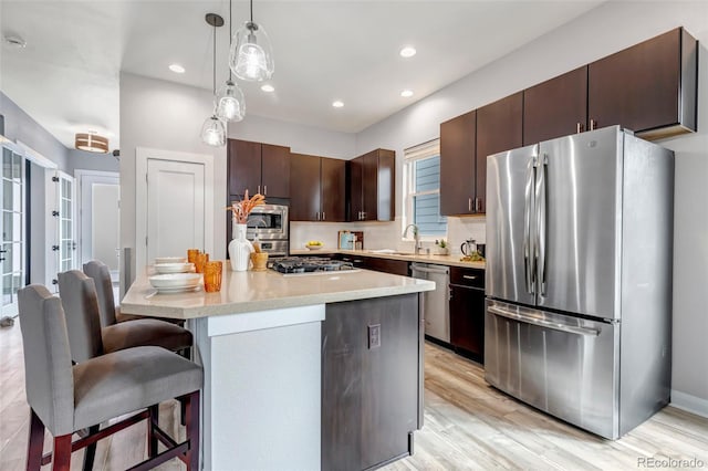 kitchen featuring decorative light fixtures, stainless steel appliances, dark brown cabinets, light countertops, and a sink