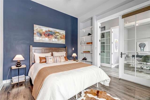 bedroom featuring an accent wall, baseboards, wood finished floors, and french doors