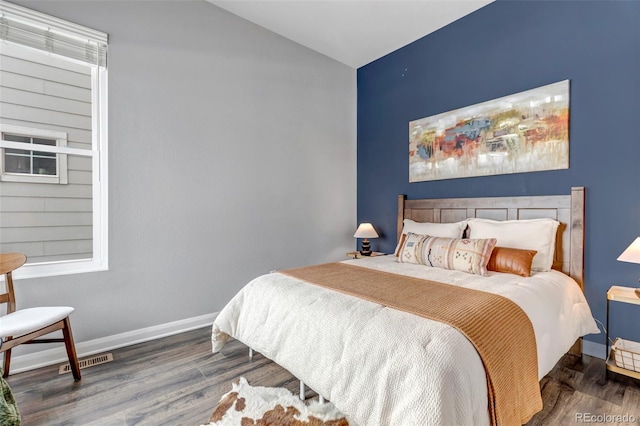 bedroom featuring lofted ceiling, visible vents, baseboards, and wood finished floors