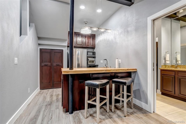 bar featuring baseboards, freestanding refrigerator, a sink, light wood-type flooring, and indoor wet bar