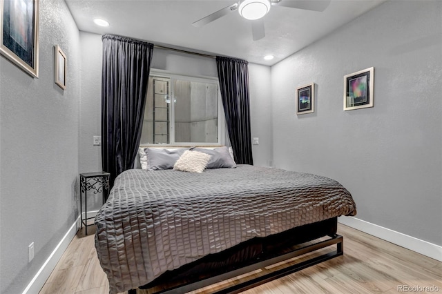 bedroom featuring a textured wall, ceiling fan, light wood-style flooring, and baseboards