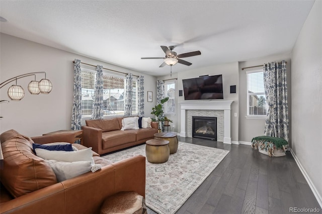 living area featuring dark wood finished floors, a glass covered fireplace, baseboards, and ceiling fan