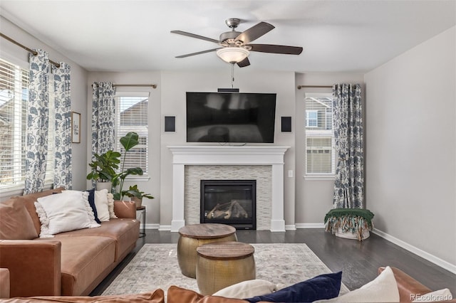 living area featuring a glass covered fireplace, dark wood-style floors, baseboards, and ceiling fan