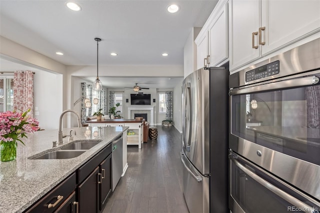 kitchen with light stone counters, dark wood-style floors, a sink, stainless steel appliances, and white cabinets