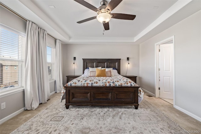 bedroom featuring a raised ceiling, light colored carpet, and baseboards