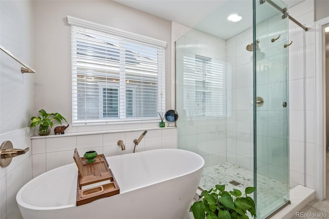 bathroom with a shower stall, a freestanding bath, and tile walls