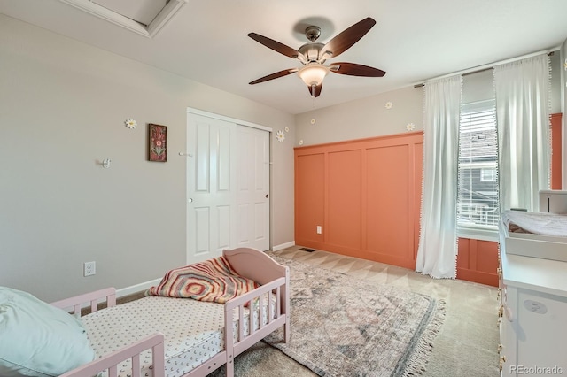 bedroom with a closet, light colored carpet, baseboards, and a ceiling fan