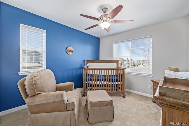 carpeted bedroom featuring baseboards, a crib, and a ceiling fan