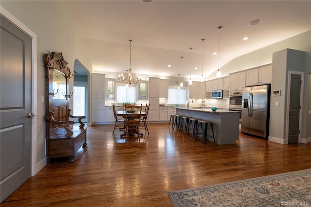 kitchen with stainless steel appliances, a center island, dark hardwood / wood-style floors, hanging light fixtures, and a breakfast bar area