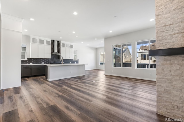 kitchen with wall chimney exhaust hood, an island with sink, dark hardwood / wood-style flooring, and white cabinetry