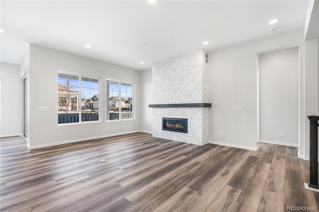 unfurnished living room with dark wood-type flooring and a stone fireplace