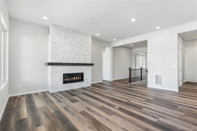 unfurnished living room with dark hardwood / wood-style flooring and a stone fireplace