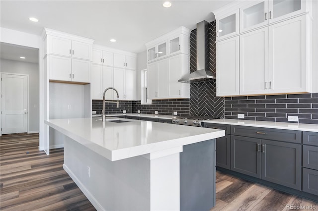 kitchen with white cabinets, sink, wall chimney range hood, and a center island with sink