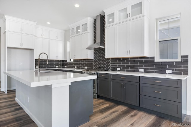 kitchen featuring stainless steel range with gas cooktop, wall chimney range hood, white cabinets, and sink