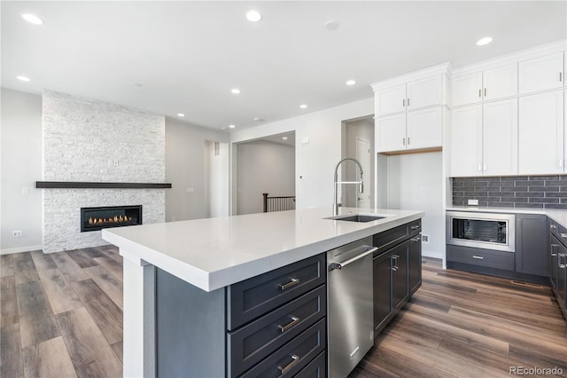 kitchen featuring white cabinetry, dark hardwood / wood-style flooring, a stone fireplace, sink, and a center island with sink