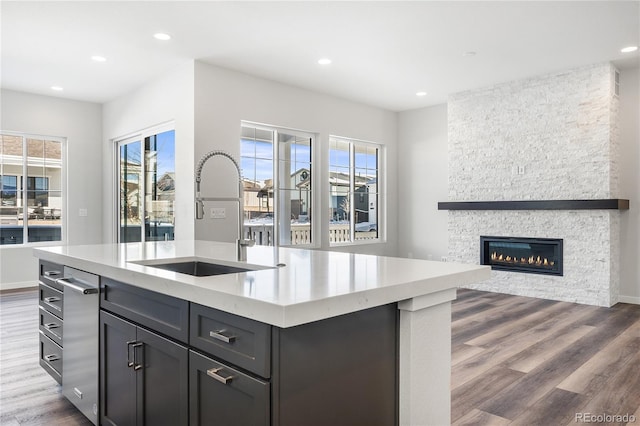 kitchen with dark wood-type flooring, a fireplace, sink, and a center island with sink