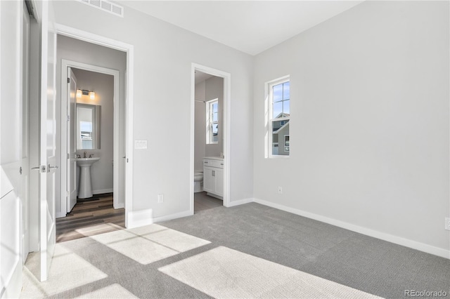 unfurnished bedroom featuring connected bathroom, dark carpet, and sink