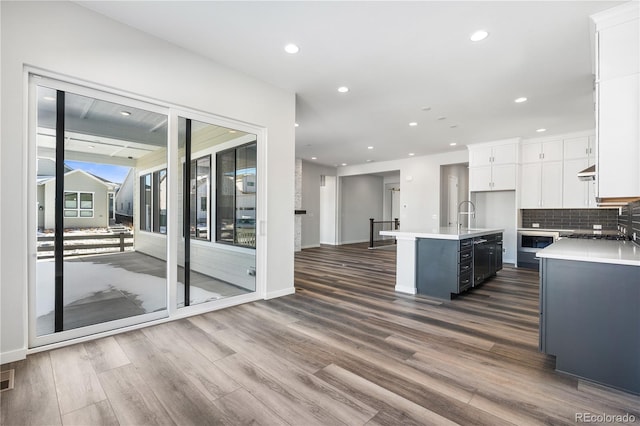 kitchen with exhaust hood, sink, a kitchen island with sink, white cabinets, and dark hardwood / wood-style flooring