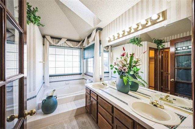 bathroom featuring lofted ceiling, a textured ceiling, tiled tub, and vanity