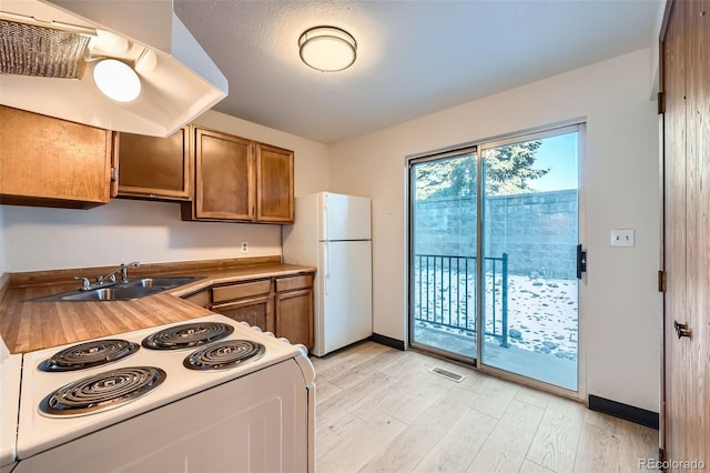 kitchen with sink, a textured ceiling, white appliances, and light hardwood / wood-style flooring