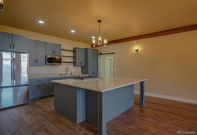 kitchen featuring dark wood-type flooring, hanging light fixtures, a barn door, a kitchen island, and stainless steel appliances