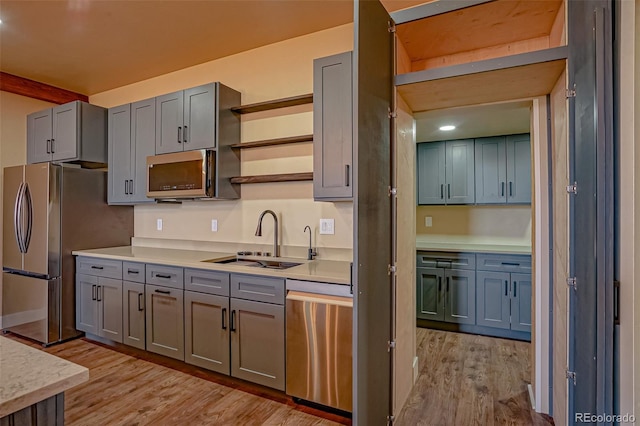 kitchen with gray cabinetry, stainless steel appliances, light hardwood / wood-style floors, and sink