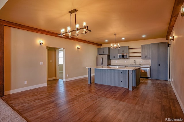 kitchen with gray cabinetry, hanging light fixtures, appliances with stainless steel finishes, a kitchen island, and wood-type flooring